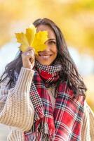 un' bellissimo sorridente donna nel autunno Abiti detiene un' giallo caduto foglia Il prossimo per sua viso foto