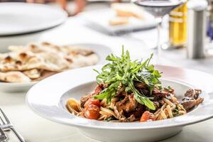 linguine con pomodori e tenero Manzo carne servito nel un' piatto e sormontato con razzo insalata foto