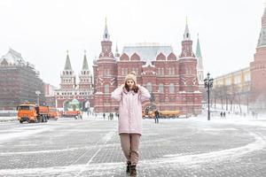 una bella ragazza con una giacca rosa cammina lungo la piazza Manezhnaya a Mosca durante una nevicata