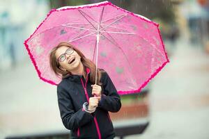 ritratto di contento bellissimo giovane pre-teen ragazza con rosa ombrello sotto pioggia. foto