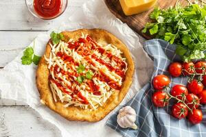 gustoso fritta langos servito su cottura al forno carta con un' lotto di grattugiato formaggio, ketchup, fresco erbe aromatiche e pomodori su un' verificato piatto stoffa foto