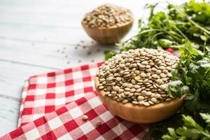 crudo Lenticchie nel di legno bocce con prezzemolo erbe aromatiche su cucina tavolo foto