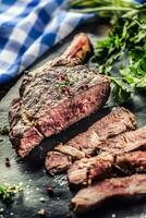 appena grigliato tomahawk bistecca su ardesia piatto con sale Pepe rosmarino e prezzemolo erbe aromatiche. affettato pezzi di succoso Manzo bistecca foto