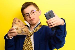 bambino ricco e di successo che si fa un selfie con i soldi, ritratto di un ragazzo in abito su uno sfondo giallo. foto