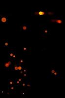 bokeh arancione su sfondo nero, scintille brucianti e sfocate dal fuoco. particelle di brace ardente volano e brillano isolate nel cielo notturno. foto