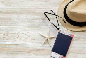 superiore Visualizza di cannuccia cappello, occhiali, blu passaporto e stella marina su di legno tavolo. estate spiaggia e vacanza viaggio concetto con copia spazio. foto