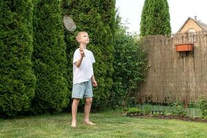 un' contento ragazzo detiene un' badminton racchetta nel il suo mani, giocando gli sport al di fuori nel estate foto