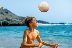 giovane ragazzo giocando con un' calcio palla su il spiaggia di il mare foto