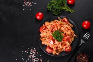deliziosa pasta fresca con salsa di pomodoro con spezie ed erbe aromatiche su sfondo scuro foto
