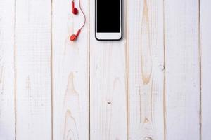 smart phone e auricolare rosso sul tavolo di legno bianco foto