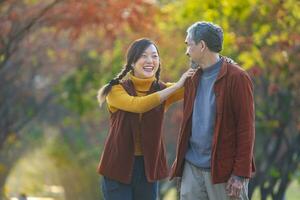 contento asiatico famiglia a piedi insieme nel il pubblico parco durante con autunno colore a partire dal acero e ginkgo albero durante autunno stagione foto