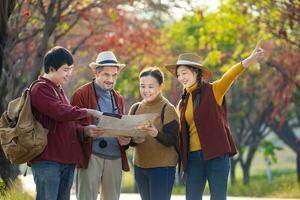 contento asiatico famiglia con anziano genitore a piedi insieme nel pubblico parco durante autunno con acero e ginkgo albero mentre guardare a carta geografica per autunno colore viaggio destinazione e famiglia contento vacanza foto