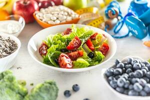 salutare fresco insalata con pomodori olive e oliva olio, circondato di salutare cibo e esercizio attrezzatura foto