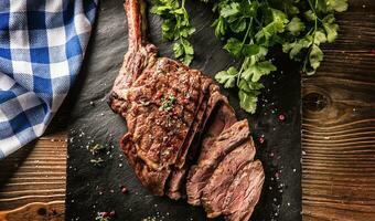 appena grigliato tomahawk bistecca su ardesia piatto con sale Pepe rosmarino e prezzemolo erbe aromatiche. affettato pezzi di succoso Manzo bistecca foto