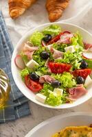 salutare insalata nel un' ciotola con olive, ravanelli, pomodoro, formaggio e magro prosciutto servito per prima colazione foto