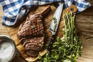 appena grigliato tomahawk bistecca su ardesia piatto con sale Pepe rosmarino e prezzemolo erbe aromatiche. affettato pezzi di succoso Manzo bistecca foto