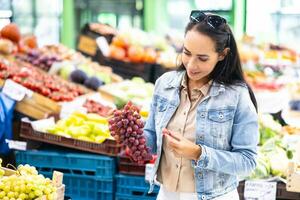 donna scelte uno uva a partire dal un' mazzo di rosso vino nel sua mani nel il mercato foto