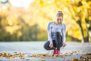 donna corridore legatura lacci delle scarpe prima jogging nel autunno albero vicolo parco. gli sport femmina autunno attrezzatura ghette e termico biancheria intima foto