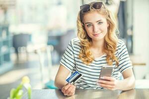 giovane donna nel il bar Tenere credito carta e utilizzando cellula, inteligente Telefono per in linea shopping foto