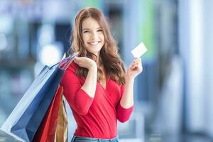 bellissimo contento ragazza con credito carta e shopping borse nel shopping centro commerciale. shopping centro nel il sfondo. foto
