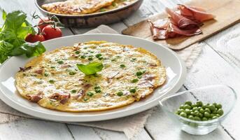 frittata con prosciutto piselli basilico pomodori e erbe aromatiche su bianca piatto foto