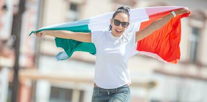 contento giovane donna celebra vittoria di Italia su un' strada Tenere un' bandiera e salto a partire dal gioia foto