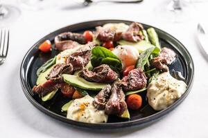 colorato insalata con fianco bistecca Riempimento il buio piatto su un' ristorante tavolo foto