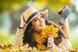 sorridente femmina detiene sua cappello e caduto le foglie nel sua mani su un autunno giorno foto