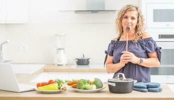 ritratto di contento adulto donna nel sua moderno cucina con pentola e verdure foto