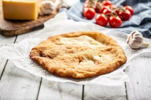 tradizionale ungherese piatto langos servito su un' cottura al forno carta nel il sfondo con aglio pomodori e formaggio su un' di legno piatto foto