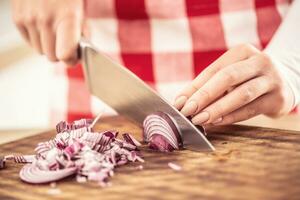 dettaglio di femmina mani taglio un' rosso cipolla su un' chopping tavola foto