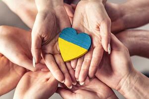 noi In piedi con Ucraina simbolo come numerose mani hold uno un altro nel unità con un' di legno cuore dipinto nel ucraino bandiera colori su superiore foto