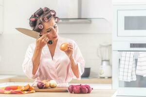 ragazza grida al di sopra di cipolla chopping nel il cucina indossare testa bigodini nel il cucina foto