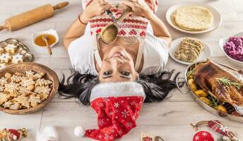 indietro Visualizza di un' femmina cucinare nel un' Natale grembiule e Santa cappello dire bugie su il terra circondato di Pan di zenzero, linz torte, a partire dal il altro lato, arrosto Oca o tacchino con lato piatti foto