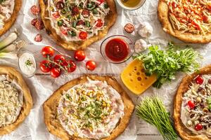 un' vicino su un' impostato di ungherese tradizionale langos con croccante aglio bordi servito con la verdura, crema salsicce, erbe aromatiche, grattugiato, formaggio, ketchup e tuffi foto