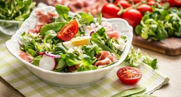 fresco primavera insalata con verde le foglie pomodori uovo ravanello rosso cipolla giovane piselli prosciutto feta formaggio e oliva olio foto