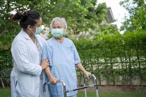 il medico aiuta e cura la donna anziana o anziana asiatica anziana usa il camminatore con una buona salute mentre cammina al parco in una felice vacanza fresca foto