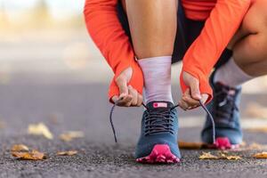 giovane femmina atleta legatura lacci delle scarpe prima in esecuzione nel autunno parco - vicino su. foto