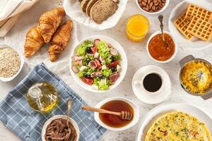 ampio assortimento di cibo Compreso frittata, Cornetti, insalata, pane, fiocchi d'avena, marmellata, cialde, Miele, cioccolato differenza, caffè e arancia succo servito su un' tavolo foto