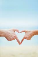 Due persone fabbricazione un' cuore forma con loro mani su il spiaggia foto
