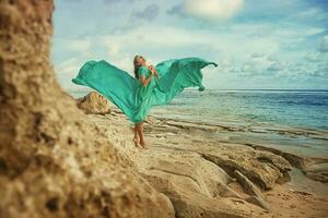 un' donna nel un' verde vestito in piedi su un' roccioso spiaggia foto