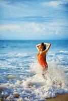 un' donna nel un arancia costume da bagno è spruzzi nel il oceano foto