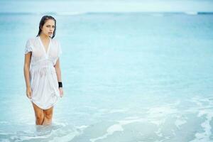 un' donna nel un' bianca vestito in piedi nel il oceano foto