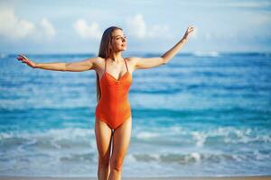 un' donna nel un arancia costume da bagno in piedi su il spiaggia foto