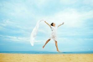 un' donna nel bianca vestito salto su il spiaggia foto