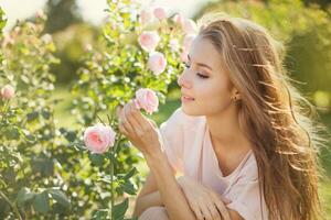 bellissimo giovane donna odorare Rose nel il giardino foto