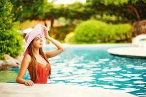 un' donna nel un' costume da bagno e cappello in piedi di un' piscina foto