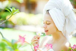 un' donna nel un' asciugamano è odorare fiori foto
