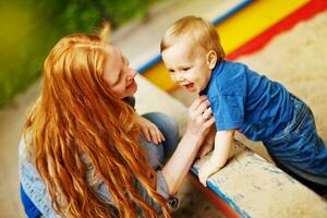 un' donna e un' bambino giocando nel un' sandbox foto