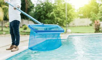 uomo pulizia il piscina con il schiumarola, un' uomo pulizia piscina con foglia schiumatoio. persona con scrematrice pulizia piscina, mani Tenere un' scrematrice con blu piscina nel il sfondo foto